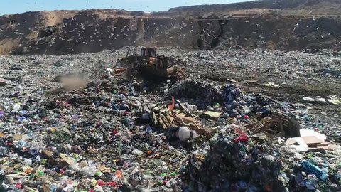 Top view of an open city garbage dump. Birds fly, a bulldozer levels piles of garbage, aerial photography. Concept: environmental problems of the city, landfill for the disposal of human waste.
