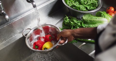 African american female chef washing vegetables in colander in restaurant kitchen. working in a busy restaurant kitchen.