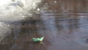Early spring landscape. Melting winter snow turning into much water on sidewalks. 4k stock video footage of one cute small paper green boat floating on surface of spring water puddle.