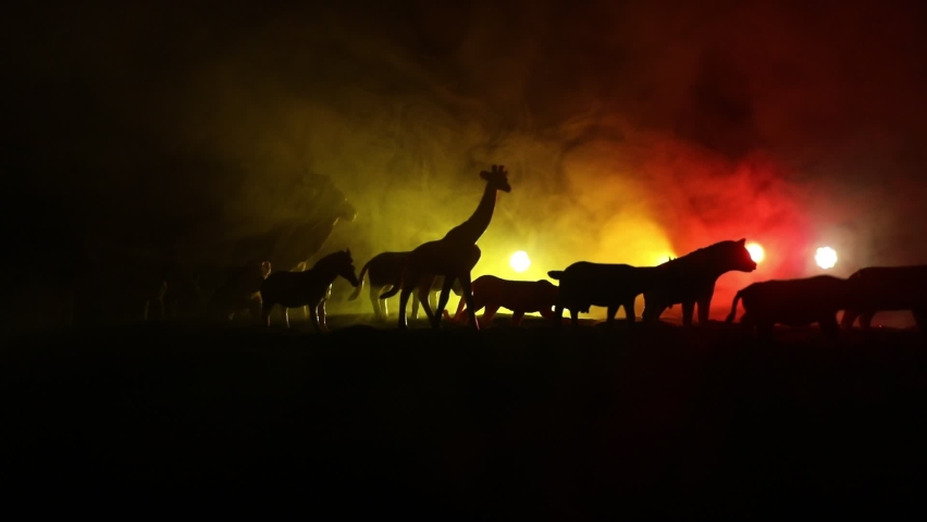 A group of animals are grouped together at foggy night with burning colorful background. Animals Running Escaping to Save Their Lives from fire. Selective focus.