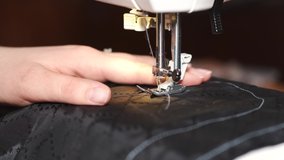 A woman sews on a sewing machine. Black cloth. Profession. Work in the Studio. White machine. The view from the top. Close-up. 4K video