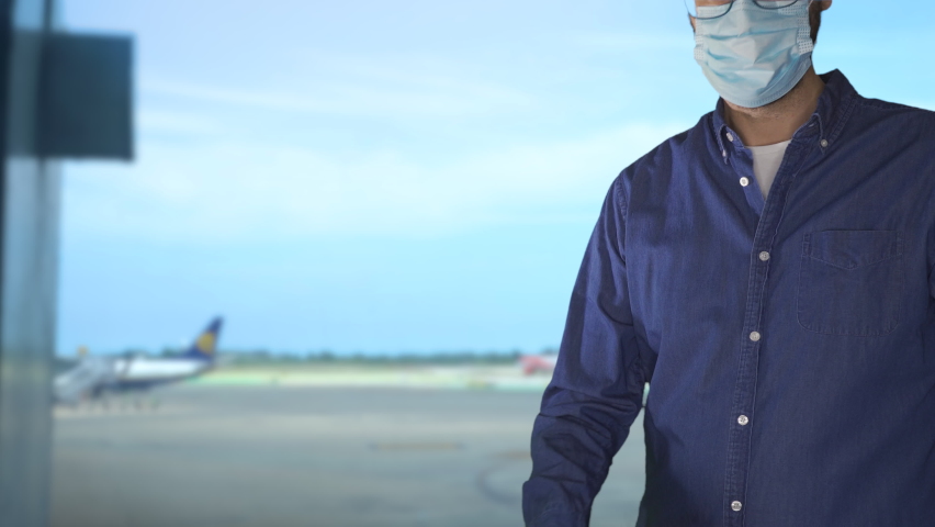 unidentified man wearing a face mask and holding a passport and a Green pass with meaningless QR code representing a certificate of vaccination.Airport on the background. Royalty-Free Stock Footage #1068736751