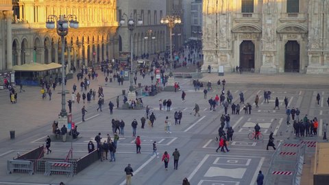 Beautiful views of Piazza Duomo and the Cathedral at sunset. Tourists and locals for a walk. A bouquet of red roses on the balcony table. Luxurious life Dolce Vita. Blue sky. Milan Italy February 2021
