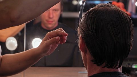 Back view professional hairdresser preparing cutting hair behind ears making stylish haircut to a young guy while he looks at himself in the mirror. High quality 4k resolution footage. 