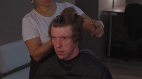 Asian ethnicity hairdresser woman parts in sections mans head to trims back of his head pulling his hair cuts off the ends. High quality 4k resolution footage. 