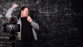 Algebra teacher dances on chalkboard background with formulas and equation in front of mobile camera. A professor takes a break during an online lesson. A funny man is recreating at distance education - Powered by Shutterstock - Get 15% off with code: PIKWIZARD15