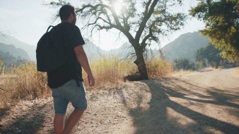 Malibu creek park, June 2020. Back view on person with backpack hiking in dry forest on hot summer day. Adult men in 30s walking by nature park and pointing on the wild animal running by the trail
