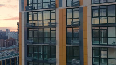 Aerial view of a newly built modern high-rise apartment building facade. Close-up elevator shot at sunset