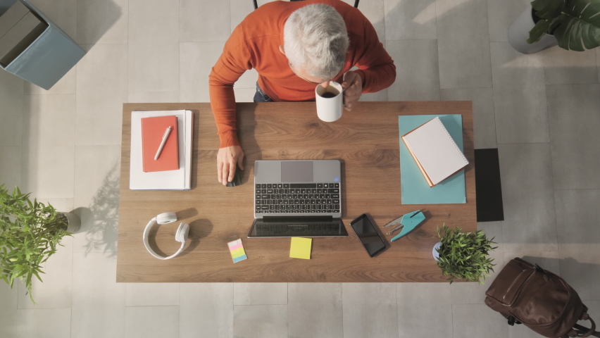 Businessman working at his desk typing on laptop computer top down view ,male entrepreneur works from home using notebook writing email and drinking coffee above shot indoors | Shutterstock HD Video #1068747824