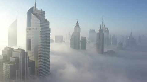 Dubai city under a could of heavy fog. Aerial view. Reveal shot. Drone coming out of clouds and show skyscrapers.