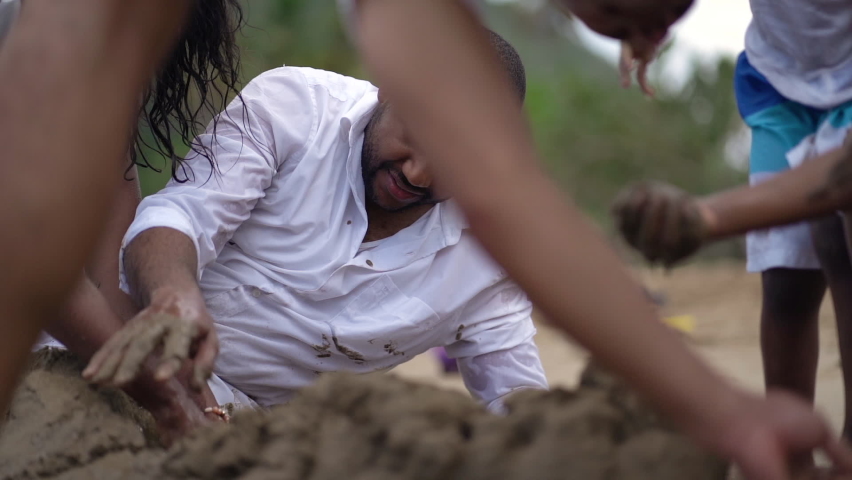 Happy African American family playing with the sand on the shore of the beach. 3 people. Father enjoying playing with his children on the beach