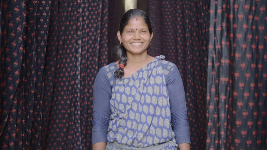 Close up shot of an Indian female daily wage laborer of  local or domestic textile dyeing firm standing around the color printed cloth materials for the drying process smiling and looking at Camera | Shutterstock HD Video #1068763442