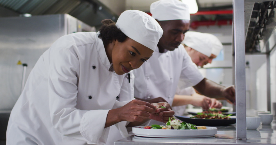 Diverse group of chefs garnishing dishes and similing in restaurant kitchen. Working in a busy restaurant kitchen.
