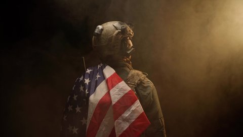 Special forces soldier standing with his back to us in the dark holding USA national flag