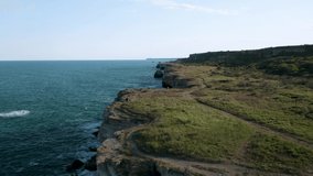 Aerial video with mother and daughter walking along picturesque rocky coastline with green fields and trees. Yailata - national archeological and nature reserve, Bulgaria.