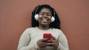 Happy Afro woman messaging online with mobile smartphone while listening music with wireless headphones - Powered by Shutterstock - Get 15% off with code: PIKWIZARD15