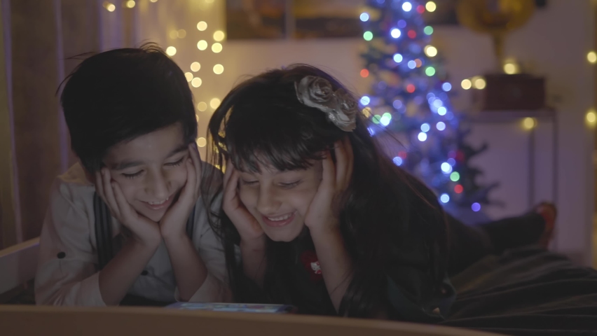 Shot of cute little dressed up Indian Asian siblings brother and sister watching cartoon movies or videos on a smartphone together with great excitement at home well-decorated home on Christmas eve Royalty-Free Stock Footage #1068773168