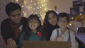 Shot of Indian Asian cheerful and close-knit family sitting on a couch talking on an online video call using laptop with great excitement at home well decorated on the occasion of Christmas eve