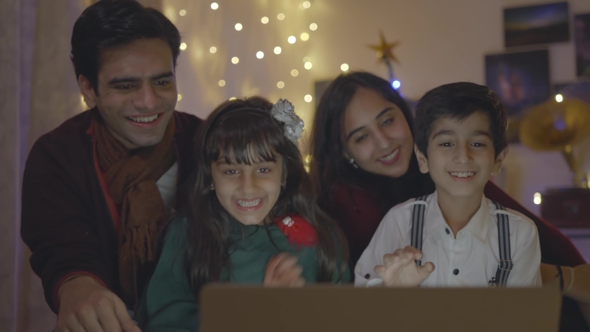 Shot of Indian Asian cheerful and close-knit family sitting on a couch talking on an online video call using laptop with great excitement at home well decorated on the occasion of Christmas eve Royalty-Free Stock Footage #1068773171