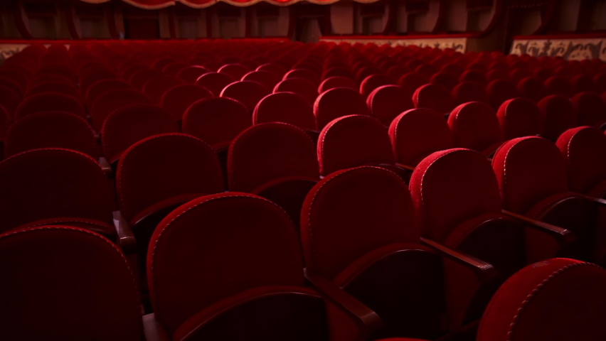 Red velvet chairs in theater hall. Rows of comfortable seats without people. Empty auditorium during pandemic. Slow motion. Royalty-Free Stock Footage #1068777128