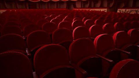Red velvet chairs in theater hall. Rows of comfortable seats without people. Empty auditorium during pandemic. Slow motion.