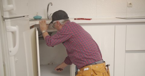 Old male plumber fixing the kitchen faucet's pipes
