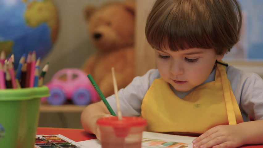 Four Year Old Caucasian Boy Having Fun Paints Picture On Paper, Being Creative and Artistic. Close Up Portrait Child Draws With Colored Paints on Paper. Cute Little Child Boy is Sitting and Painting. Royalty-Free Stock Footage #1068781055
