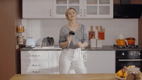 Young housewife sings and dances with the ladle in the kitchen. Young woman having fun alone. The concept of having fun alone. Slow motion video.