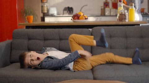 Naughty little boy on the sofa is misbehaving by jumping on the sofa. Concept of child with aggressive, hyperactive, upbringing and mental problems. Slow motion video.