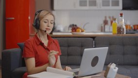 Happy young business woman wears headset talks to web camera making distance online video conference call. Female internet teacher doing distant chat working from home. Telework concept. Slow motion.
