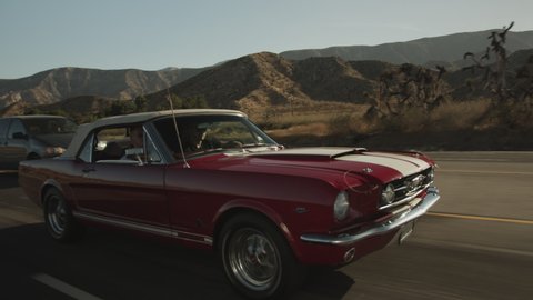 Red and White old Classic Sports Car driving on Scenic Highway in California surrounded by Desert, Tracking follow shot Palmdale, California in 2019
