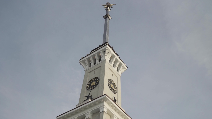 Bottom view of a clock tower with a long spire on blue cloudy sky background. Action. Details of an ancient historical building.