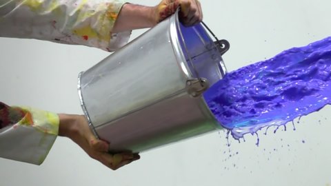 Artist hands splashing purple paint from the bucket. Painter flow the watercolor or oil ink paint to the canvas or wall. Art work in process. Drops and of color liquid fly in the air isolated on white