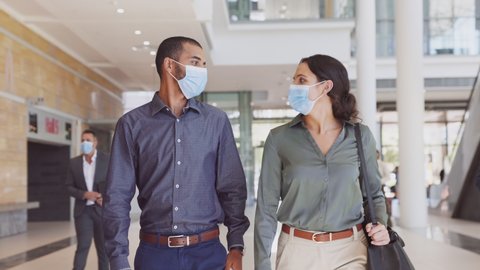 Indian business man and young businesswoman talking with face mask in the hallway of a business company. Business colleagues walking to the meeting while wearing protective face mask during covid19.