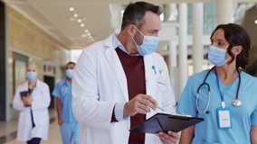 Mature doctor and nurse wearing safety mask for Covid-19 having a discussion in hospital hallway. Healthcare specialist showing medical report to nurse wearing face mask for protection against covid. - Powered by Shutterstock - Get 15% off with code: PIKWIZARD15