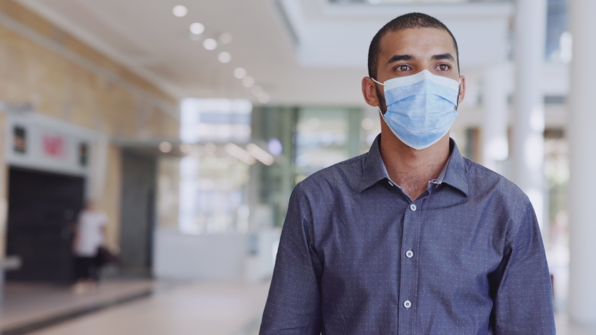Indian businessman walking in a building while taking off protective face mask and looking at camera after immunization from Covid19. Middle eastern man removing mask from face after vaccine shot. Royalty-Free Stock Footage #1068792200