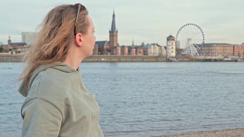 [4k] blonde woman wearing sunglasses doing her hair in front of old town of Düsseldorf wearing a green hoody