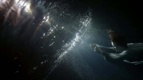 mystery and magic underwater, young woman is floating to mirror water surface, rising over surface, subaquatic slow motion shot.