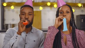 African couple having birthday video call wearing party hats and blowing party whistle. Portrait of afro-american man and woman having online birthday party on video conference