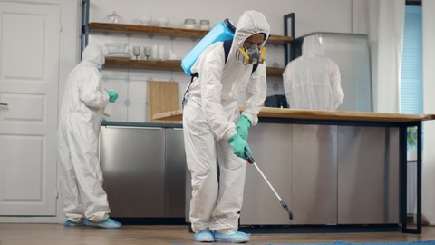 Home disinfection by commercial disinfecting services. Team of specialists in safety overall and mask disinfecting apartment with detergent spray during covid-19 epidemic
