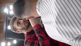 The young barber very carefully cuts the client with a trimmer. Vertical video