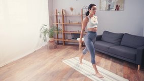 Barefoot sportswoman doing squats on fitness mat in living room