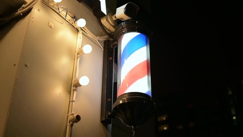 A bright barbershop sign rotates at the entrance to the barbershop in the evening. Pole spinning in the evening