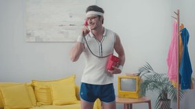 Energetic sportsman talking on landline telephone, while wagging hips at home
