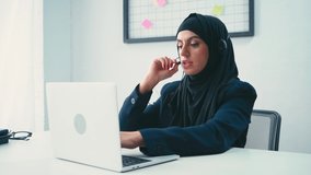 Muslim businesswoman in headset using laptop in office