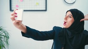 Young muslim businesswoman taking selfie on smartphone in office