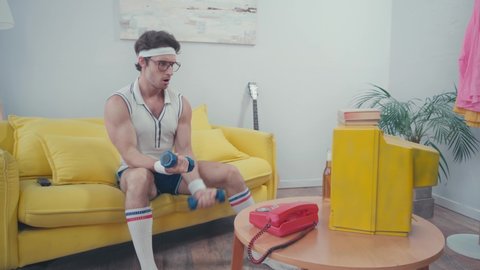 Sportsman lifting dumbbells, while watching television in living room