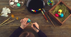 Easter christian religious holiday. Top view video of female hands painting on eggs. Artist's workshop