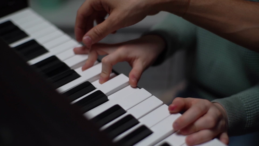Top close-up view fingers of child boy playing piano, music teacher standing near and helps with playing during lesson at school. Kid practicing piano lesson in living room. Shooting in slow motion. Royalty-Free Stock Footage #1068807191