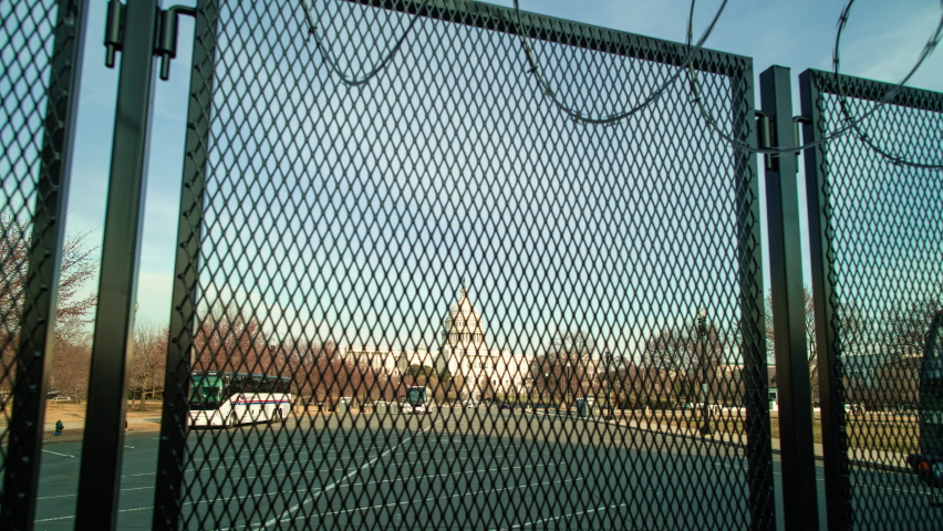 A time-lapse of the U.S. Capitol building at sunset, fortified behind a metal fence topped with razor wire to address security concerns following the January 6th 2021 insurrection. Camera dolly out.  Royalty-Free Stock Footage #1068808541